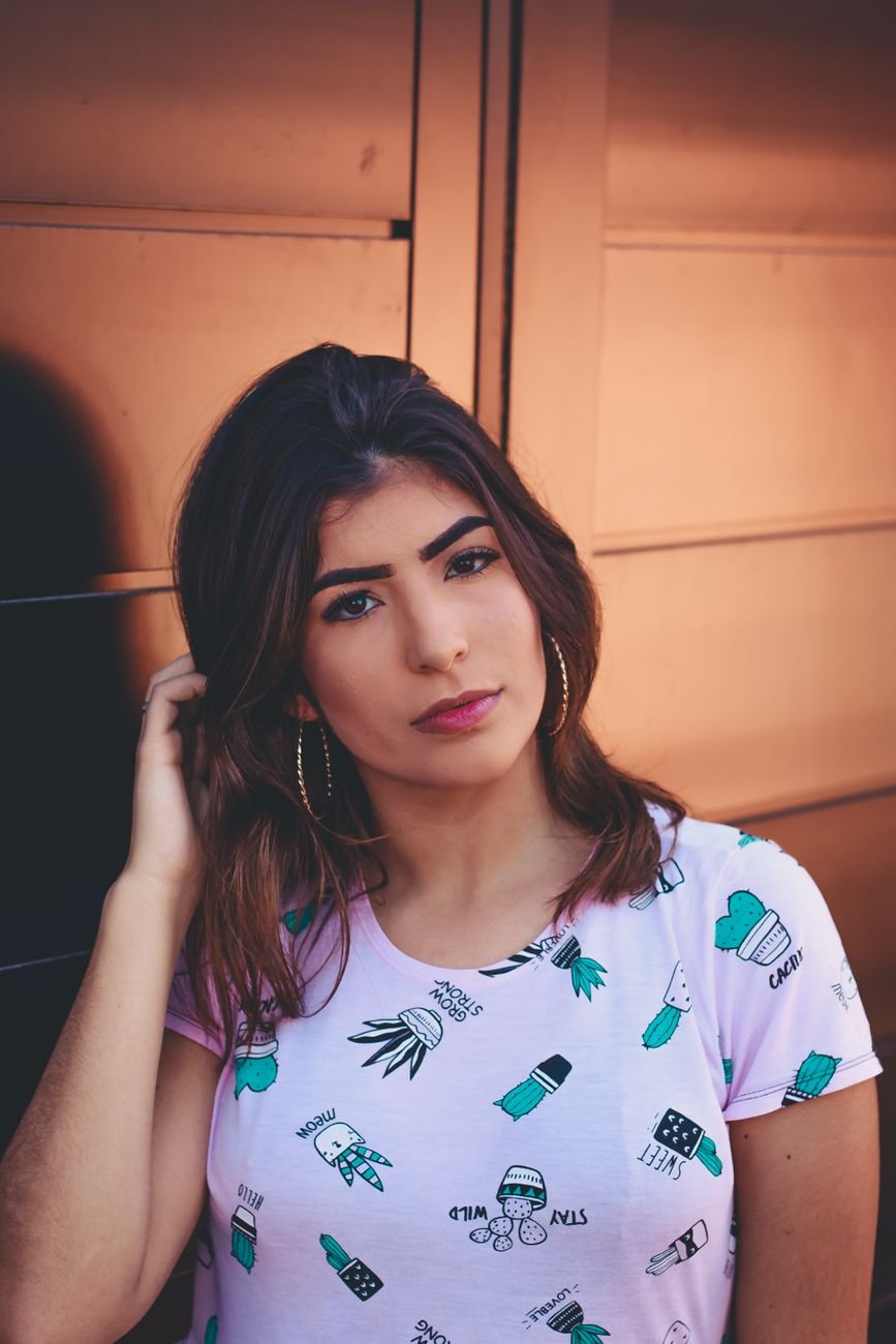 Portrait of a stylish young woman wearing a printed t-shirt, standing against a warm backdrop.